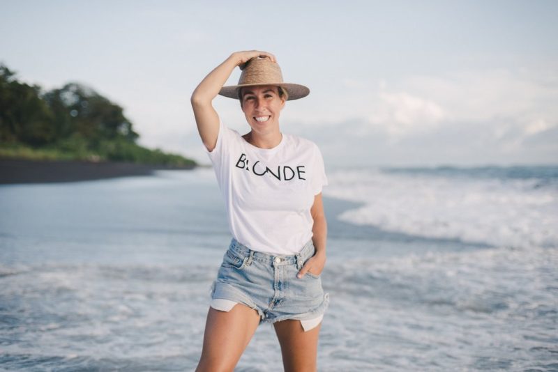 Ally Maz smiling, photographed on the beach in a white Brunette the Label tshirt.