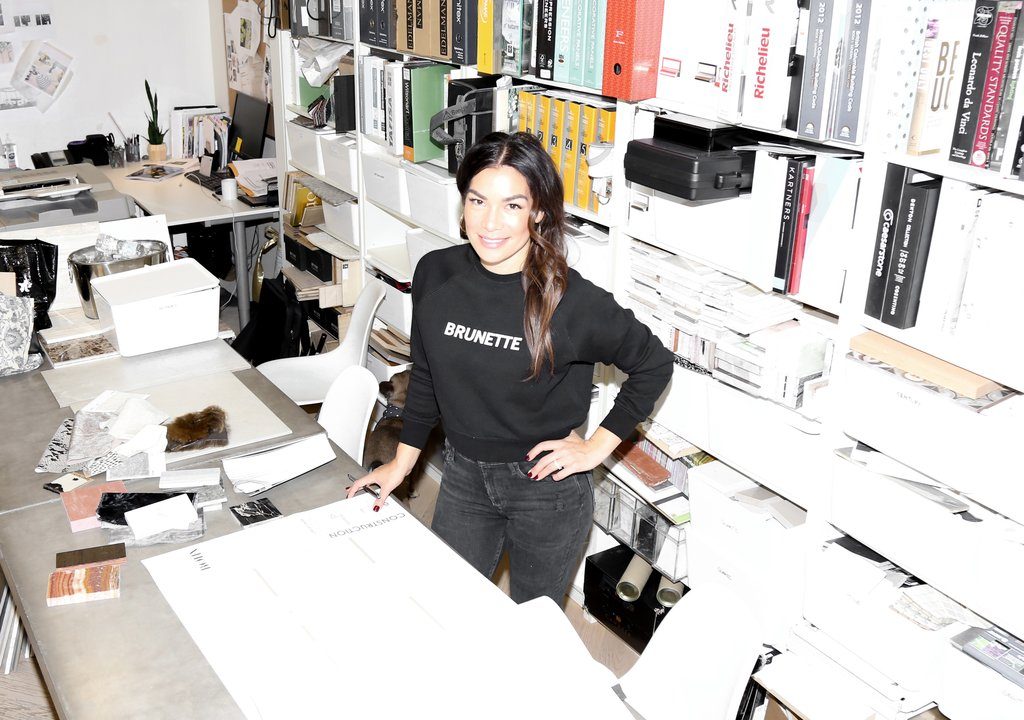 Female entrepreneur and interior designer Karin Bohn is photographed standing at her desk in a Brunette the Label sweatshirt.