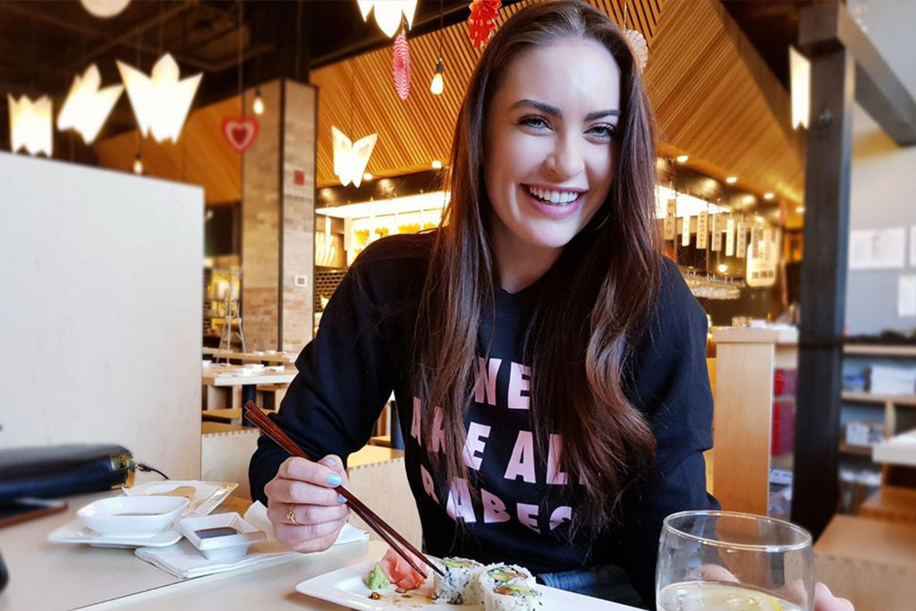 Former Miss Universe Canada and body positivity activist Siera Bearchell is photographed eating sushi and wearing the We Are All Babes Crew Neck Sweatshirt from Brunette the Label.