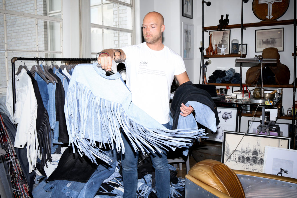 Adam Taubenfligel is photographed holding a sustainable denim jacket from his line, Triarchy.