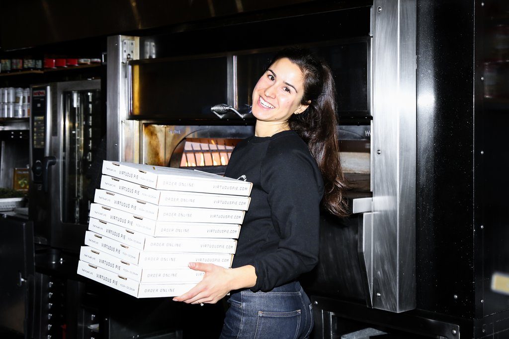 Lia Loukas is photographed holding a stack of pizza boxes from plant-based eatery Virtuous Pie. 